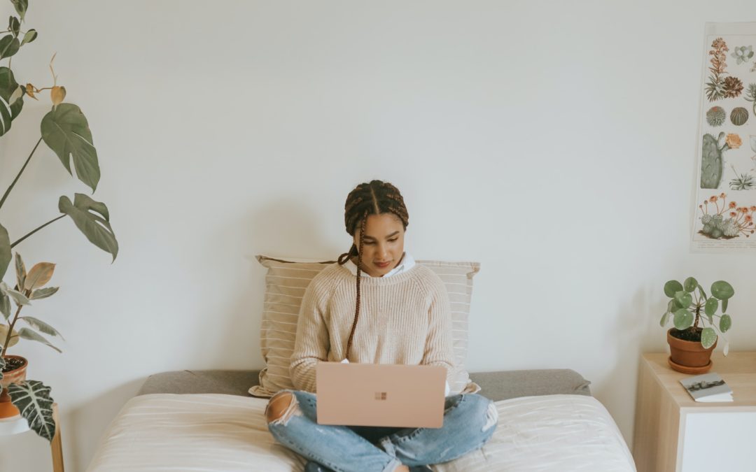 woman working on a laptop while sitting on a bed